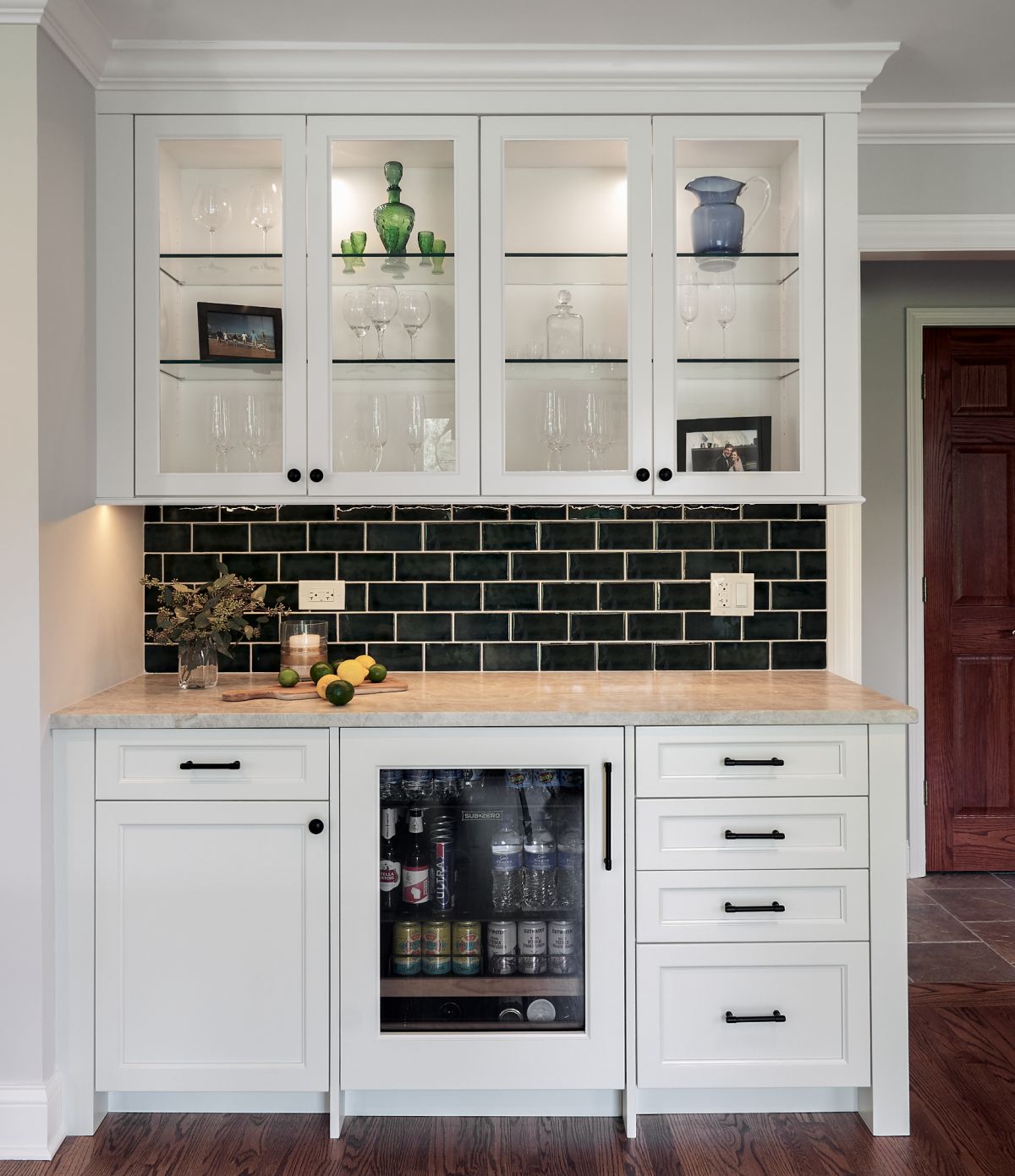 A white built-in bar cabinet with glass-front upper cabinets, a dark subway tile backsplash, and a beverage refrigerator.
