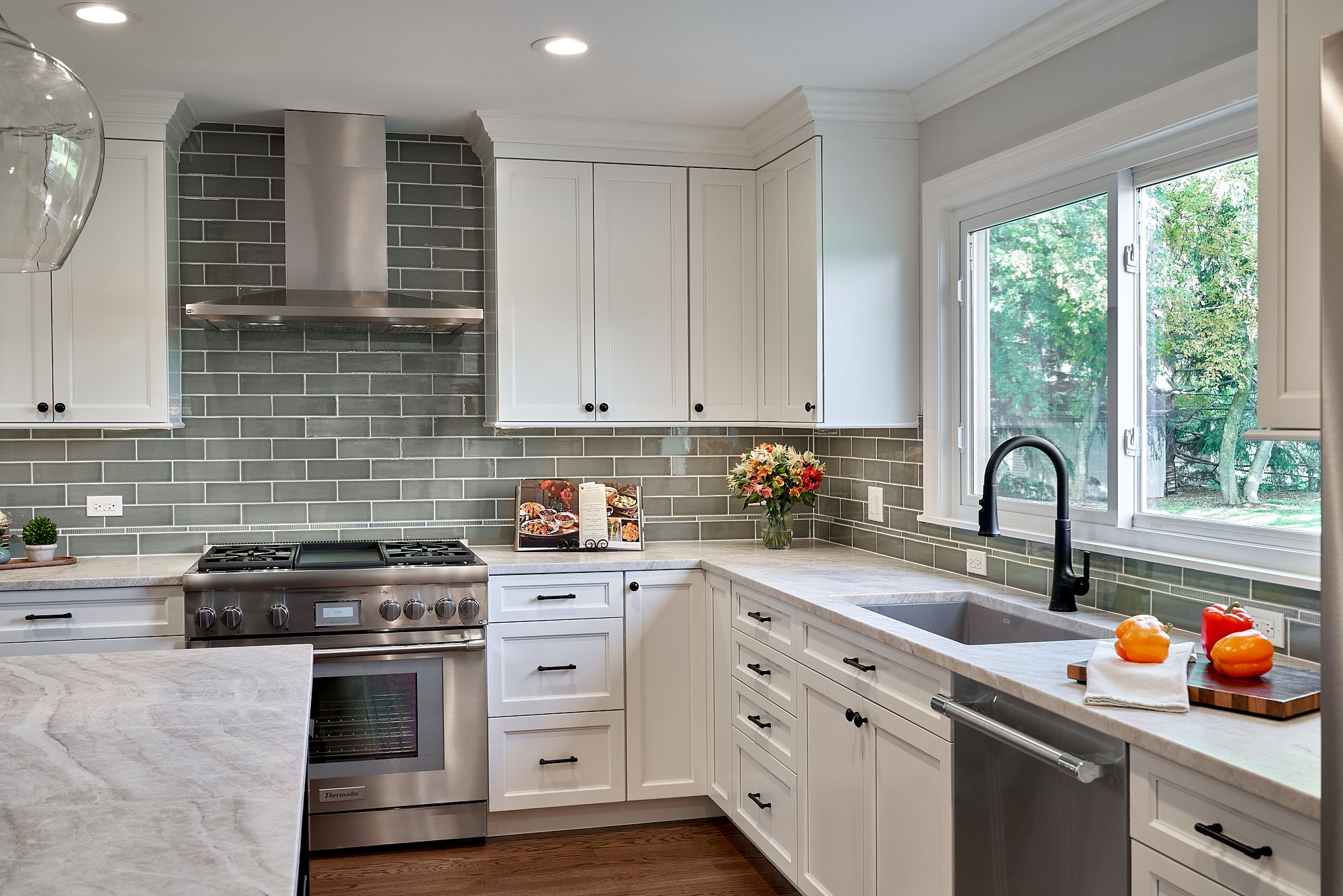 A white kitchen features a stainless steel range, hood, and appliances, with gray subway tile backsplash and light countertops.