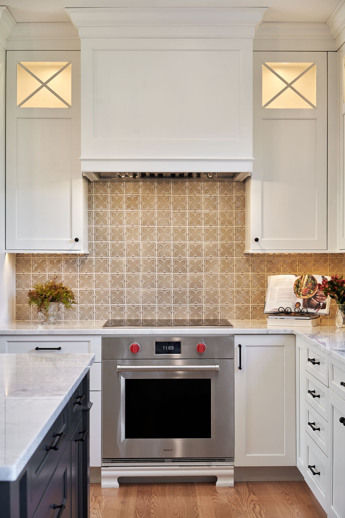 A kitchen features white upper and lower cabinets, a stainless steel oven and cooktop, and a patterned tile backsplash.