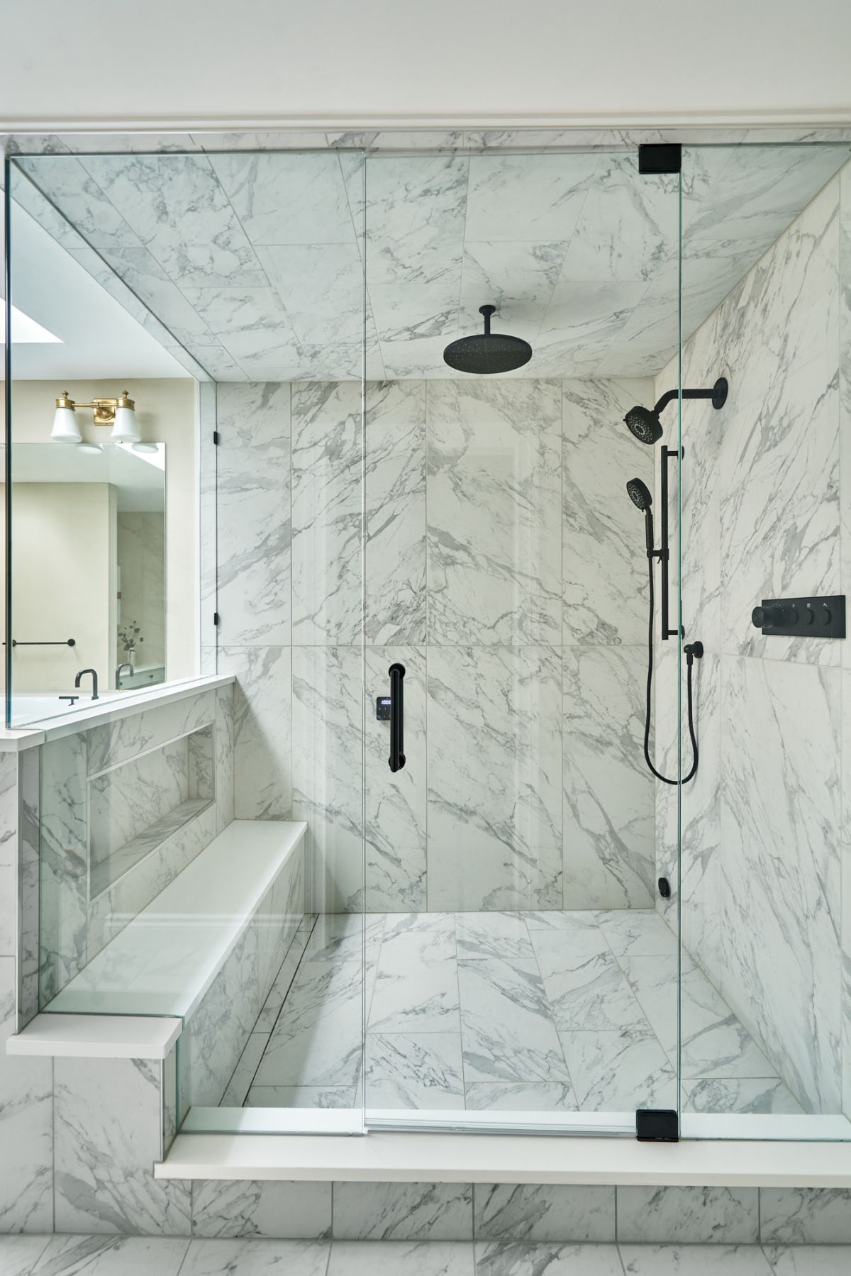 A large walk-in shower with white marble tile, a built-in bench, and black shower fixtures.