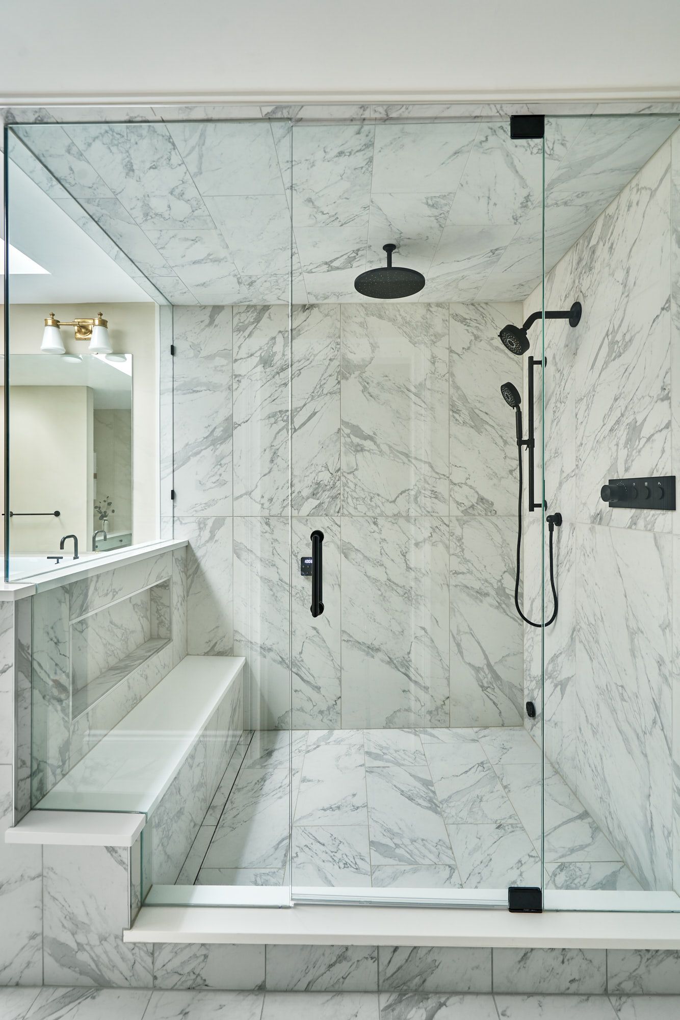 A large walk-in shower with white marble tile, a built-in bench, and black shower fixtures.